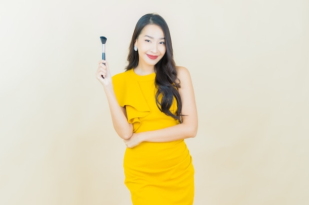 Retrato hermosa joven asiática sonríe con teléfono móvil inteligente en la pared beige
