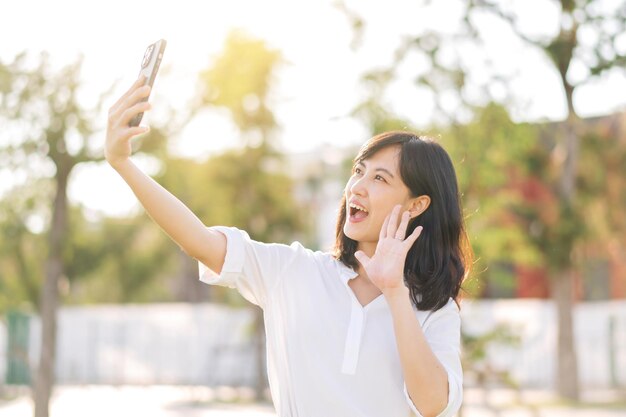 Retrato hermosa joven asiática con teléfono móvil inteligente alrededor de la vista de la naturaleza al aire libre en un día soleado de verano