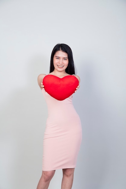 Retrato hermosa joven asiática en vestido mostrar almohada en forma de corazón aislada sobre fondo gris claro con espacio de copia