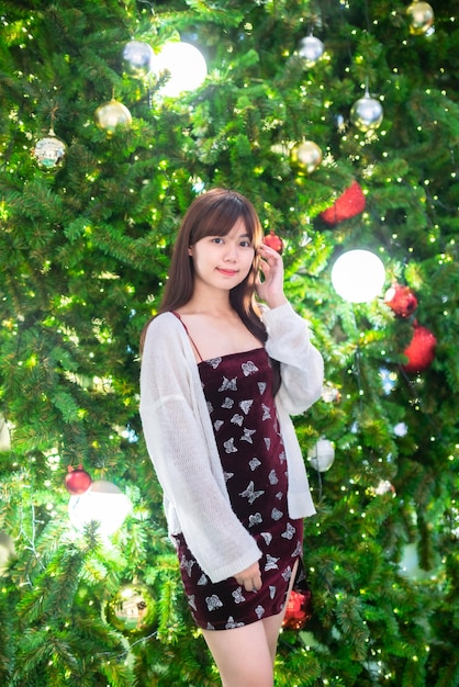 Retrato hermosa joven asiática vestido rojo traje y saludo de Navidad decoración de paquete de imagen en árbol de Navidad luz circular bokeh fondo Decoración durante Navidad y año nuevo