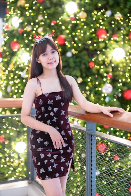 Retrato hermosa joven asiática vestido rojo traje y saludo de Navidad decoración de paquete de imagen en árbol de Navidad luz circular bokeh fondo Decoración durante Navidad y año nuevo