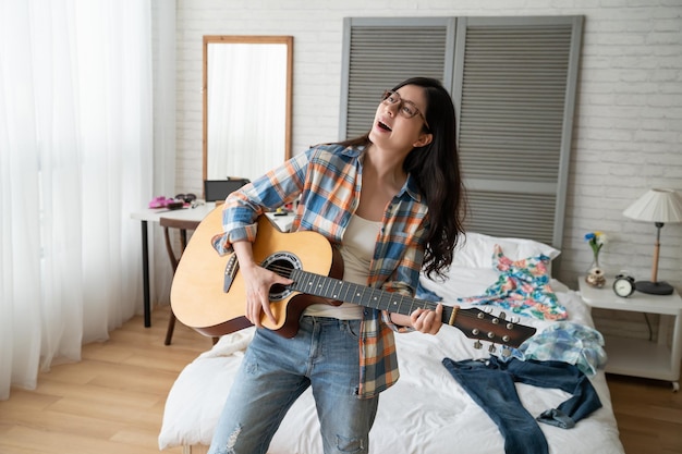 Retrato de una hermosa joven atractiva tocando la guitarra en casa. a una adolescente con gafas le encanta la música divertirse quedarse en casa en un día soleado al aire libre. elegante mujer relajada con melodía bailando dormitorio