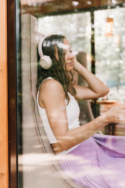 Retrato de una hermosa joven con auriculares que escucha música mientras está sentada en un café callejeroDisfruta de la generación musical Z