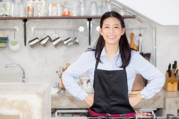 Retrato de hermosa joven barista, mujer asiática es un empleado de pie en café contador