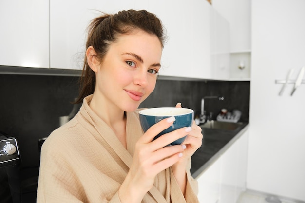 Retrato de una hermosa joven en bata de baño bebiendo café por la mañana y disfrutando del sabor sonriendo