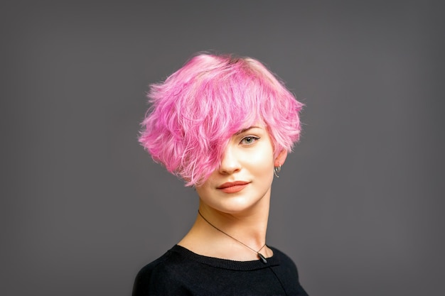 Retrato de hermosa joven blanca con un peinado corto rosa sobre fondo oscuro con espacio de copia.