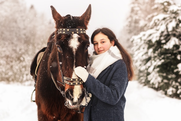 Retrato de una hermosa joven con un caballo en invierno en la naturaleza