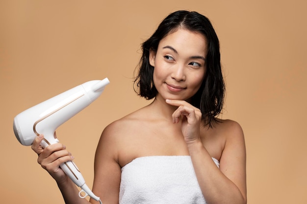 Retrato de una hermosa joven con cabello castaño sosteniendo un secador de pelo y mirándolo