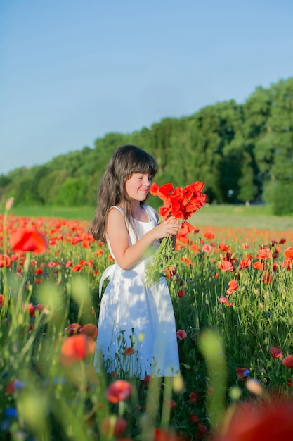 Retrato de una hermosa joven en un campo de amapolas al atardecer con ramo de amapolas