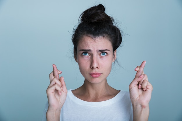 Foto retrato de una hermosa joven casual aislada sobre fondo azul, sosteniendo los dedos cruzados para la buena suerte