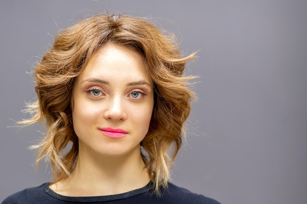 Retrato de una hermosa joven caucásica de pelo rojo con un peinado corto y ondulado sonriendo y mirando a la cámara en un fondo gris oscuro con espacio para copiar