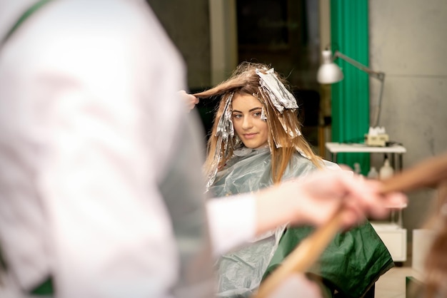 Retrato de una hermosa joven caucásica que sonríe y se tiñe el pelo con papel de aluminio en un salón de belleza