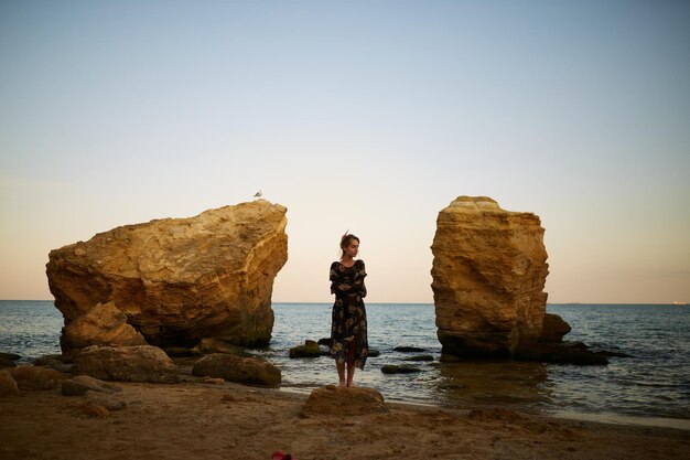 Retrato de una hermosa joven caucásica con un vestido en las rocas junto al mar con un vestido de cerca