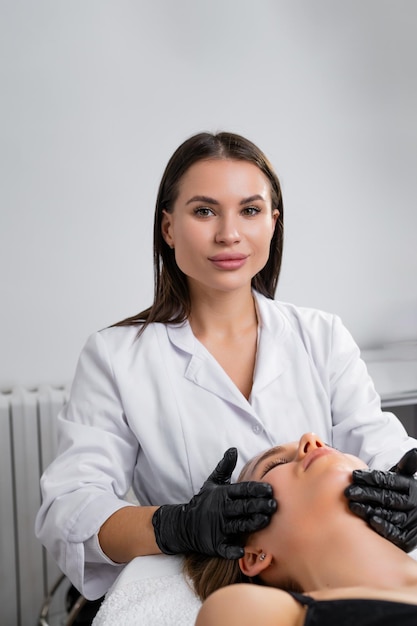 Retrato de una hermosa joven cosmetóloga que hace un masaje facial en una cosmetología