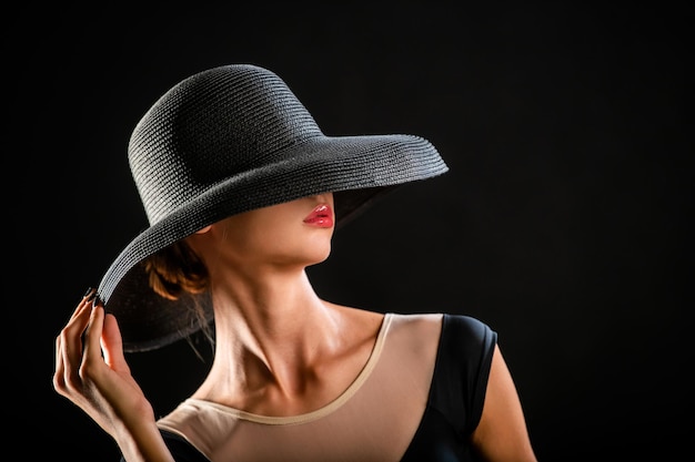 Retrato de una hermosa joven con un elegante sombrero negro sobre un fondo negro