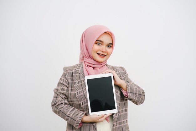 Foto retrato de una hermosa joven empresaria musulmana con un hijab rosa que indica y muestra la tableta digital sobre un fondo blanco concepto utilizable para la publicidad en teléfonos inteligentes