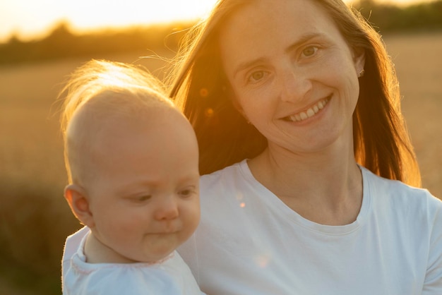 Retrato de una hermosa joven feliz con un bebé en las manos en los rayos del atardecer