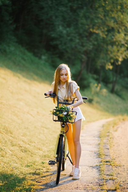 Retrato de una hermosa joven feliz con una bicicleta y flores en un fondo forestal
