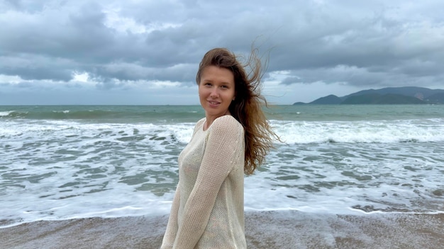 Retrato de una hermosa joven feliz positiva alegre alegre mujer disfrutando de vacaciones en el mar caminando en la playa de verano en un país tropical sonriendo divirtiéndose riendo en suéter de punto