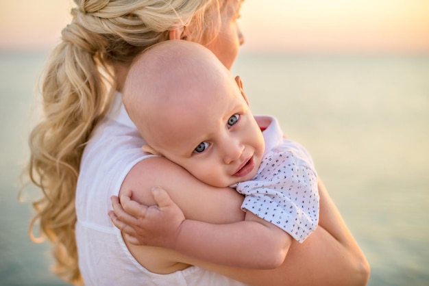 Retrato de una hermosa joven con un hijo pequeño en el fondo de una hermosa puesta de sol en el mar