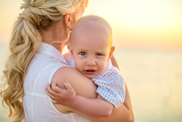 Retrato de una hermosa joven con un hijo pequeño en el fondo de una hermosa puesta de sol en el mar