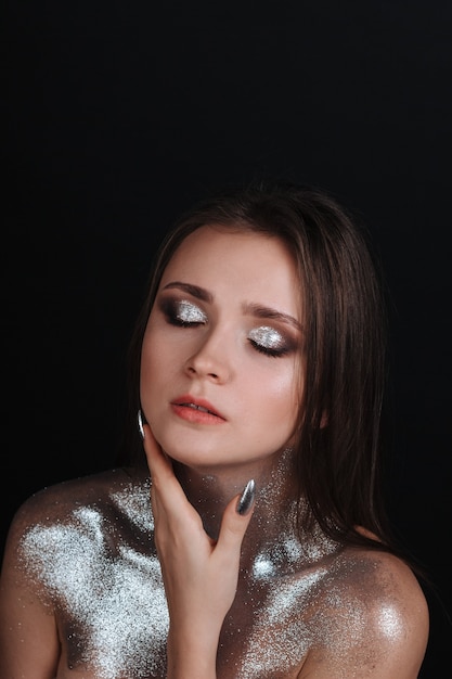 Foto retrato de una hermosa joven con lentejuelas plateadas. peinado de cabello castaño, piel limpia y bronceada, hermoso maquillaje brillante, lápiz labial rosa en los labios. la belleza del modelo facial.