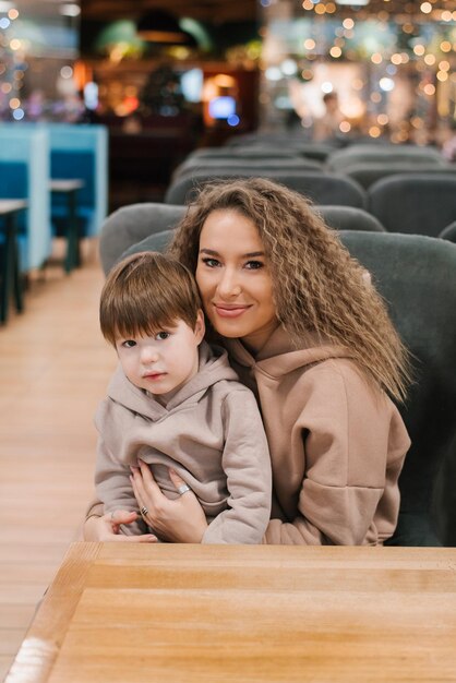 Retrato de una hermosa joven madre y un hijo de cuatro años en sus brazos La familia está sentada en una silla en un café