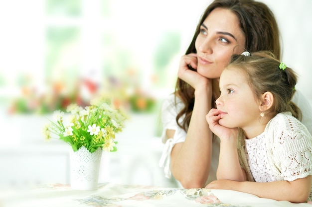 Retrato de hermosa joven madre con su linda hijita sentada en la mesa
