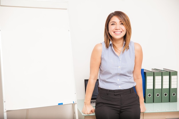 Retrato de una hermosa joven maestra apoyada en su escritorio y lista para enseñar en un salón de clases