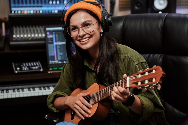 Retrato de hermosa joven morena artista femenina sonriendo a un lado tocando el ukelele mientras está sentado en