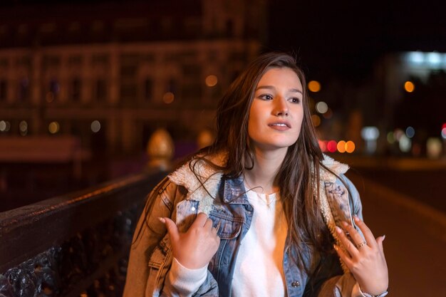 Retrato de una hermosa joven morena en el fondo de la ciudad por la noche Atractiva mujer joven en la calle de la ciudad