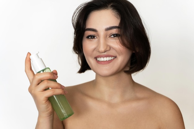 Retrato de una hermosa joven morena sonriente con una piel suave con una botella de gel limpiador