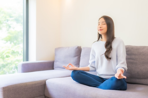 Retrato hermosa joven mujer asiática meditación en el sofá en el interior de la sala de estar