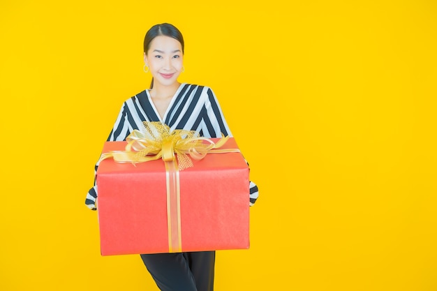 Retrato hermosa joven mujer asiática sonrisa con caja de regalo roja sobre amarillo