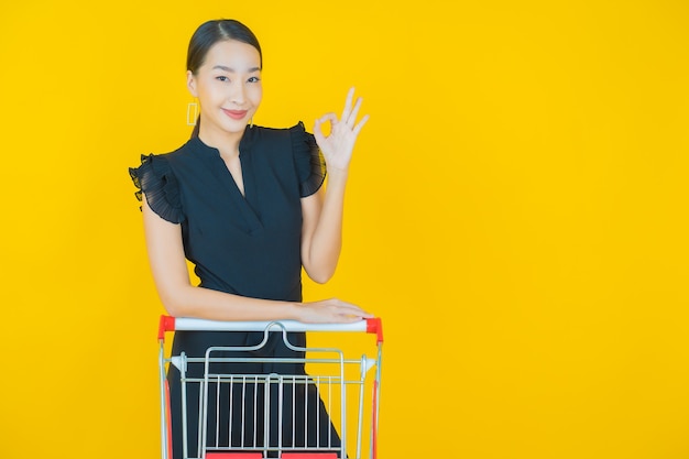 Retrato hermosa joven mujer asiática sonrisa con canasta de supermercado en amarillo