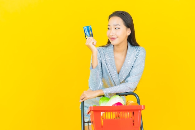 Retrato hermosa joven mujer asiática sonrisa con canasta de supermercado en pared amarilla