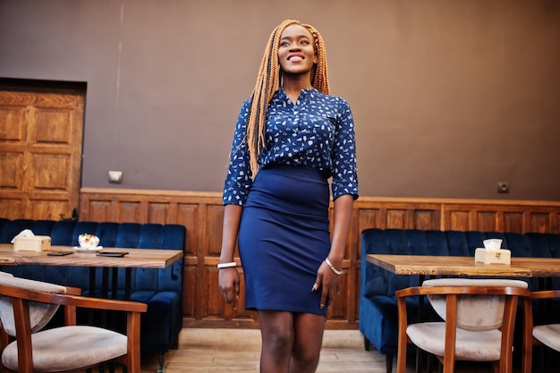 Retrato de una hermosa joven mujer de negocios africana con rastas en blusa azul y falda posada en un café