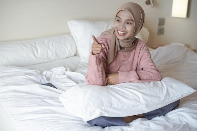 Retrato de una hermosa joven musulmana asiática con un pañuelo en la cabeza en una cama de vacaciones en un hotel