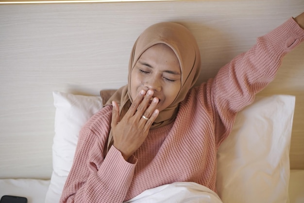 Retrato de una hermosa joven musulmana asiática que lleva un pañuelo en la cabeza mientras se acuesta en la cama y duerme