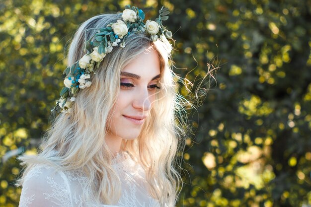 Retrato de hermosa joven novia con ramo de flores y corona en la cabeza en vestido de novia al aire libre