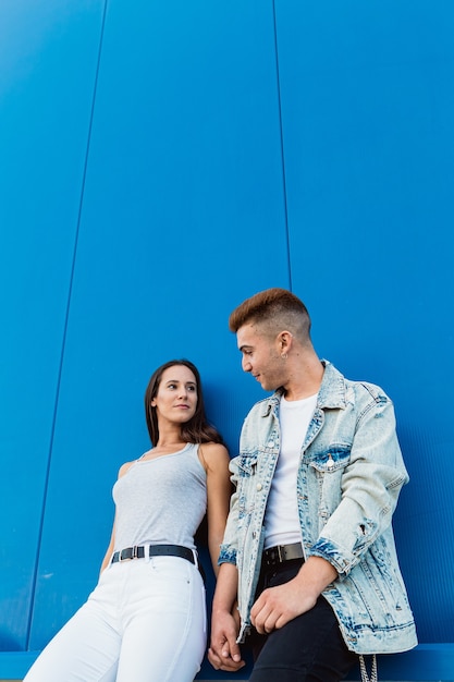 Retrato de una hermosa joven pareja de enamorados tomados de la mano con pared azul y espacio de copia