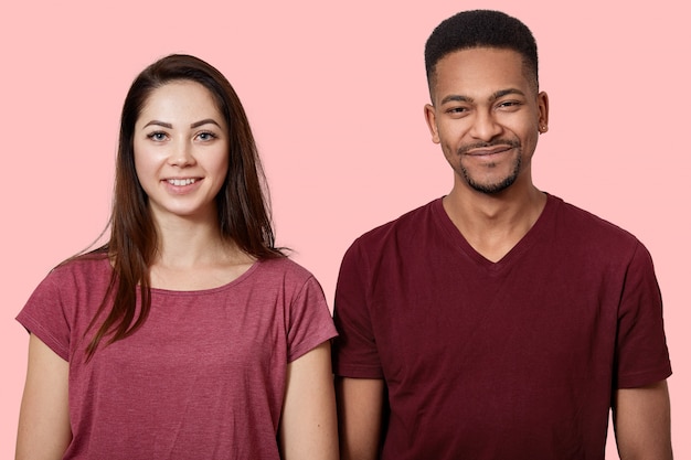 Retrato de la hermosa joven pareja mirando sonriente a la cámara, en la pared rosa