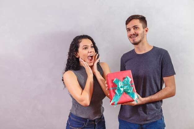 Retrato de una hermosa joven pareja en la pared gris con un regalo.