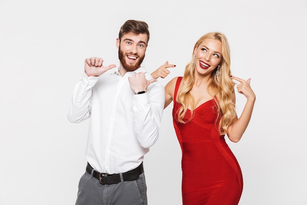 Retrato de una hermosa joven pareja vestida inteligente que se encuentran aisladas sobre blanco, celebrando el año nuevo, señalando con el dedo a una niña