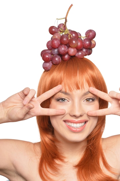 Retrato de una hermosa joven pelirroja con uvas rojas en la cabeza mostrando signos de paz