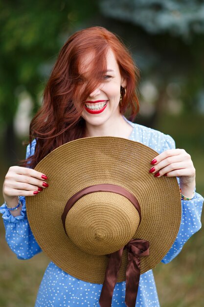 Retrato de una hermosa joven pelirroja con un vestido azul al aire libre en el parque