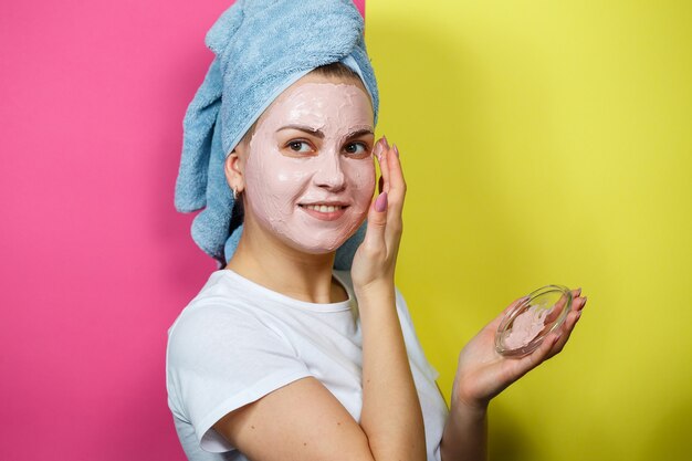 Retrato de una hermosa joven que se pone una mascarilla refrescante en el rostro para rejuvenecer y tonificar la piel. Tratamientos de belleza