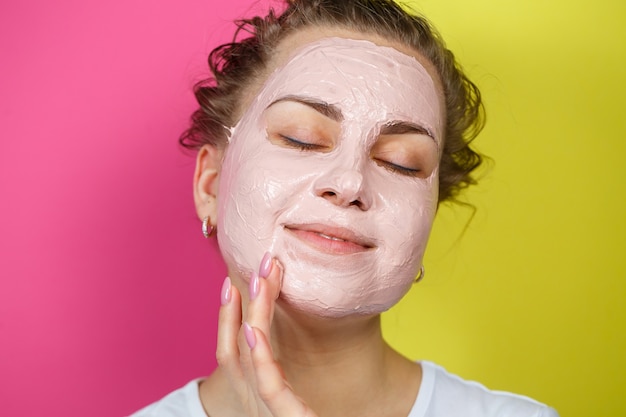 Retrato de una hermosa joven que se pone una mascarilla refrescante en el rostro para rejuvenecer y tonificar la piel. Tratamientos de belleza