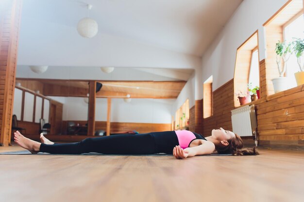 Foto retrato de una hermosa joven que trabaja descansando después de hacer ejercicios de yoga acostada en savasana cuerpo o postura de cuerpo muerto relajante