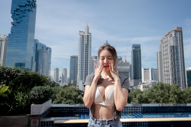 Retrato de una hermosa joven relajándose con vistas a la ciudad usando bikini blanco y jeans de pierna larga